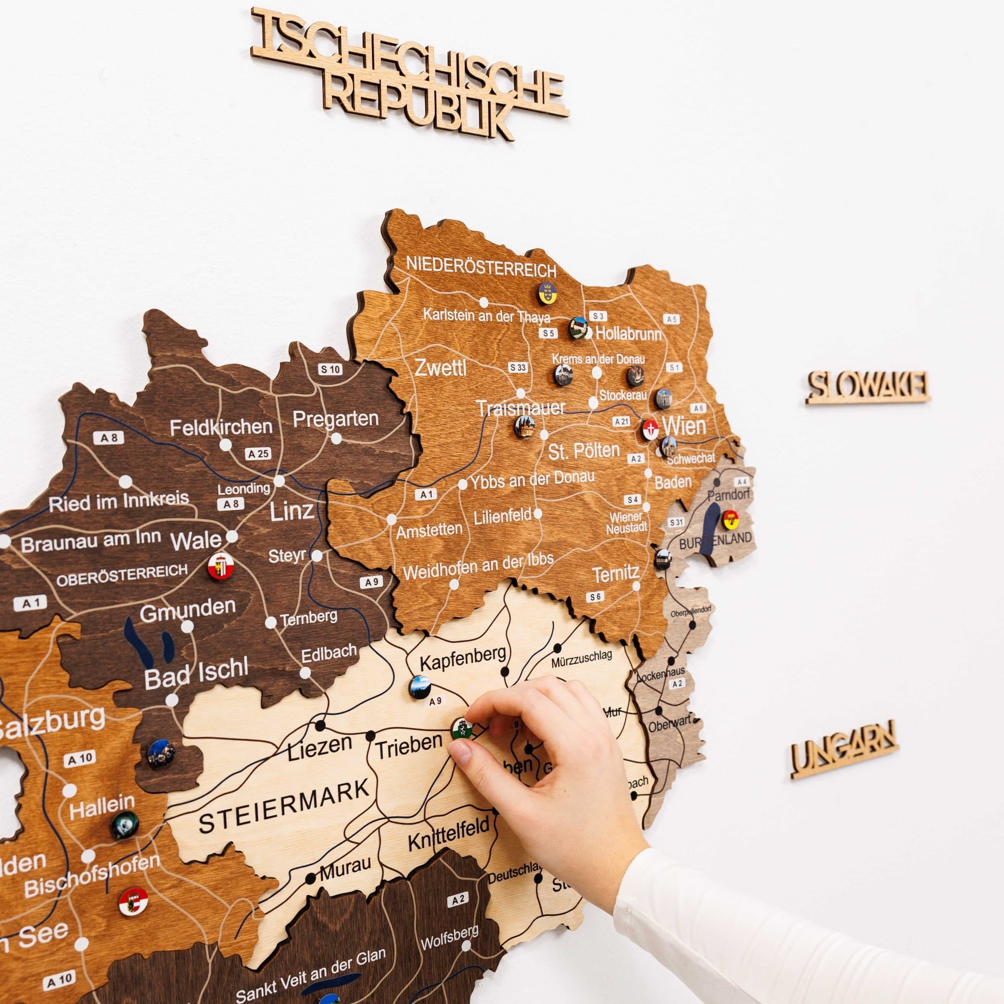 Wooden map of Austria with pushpins and a hand interacting with it.