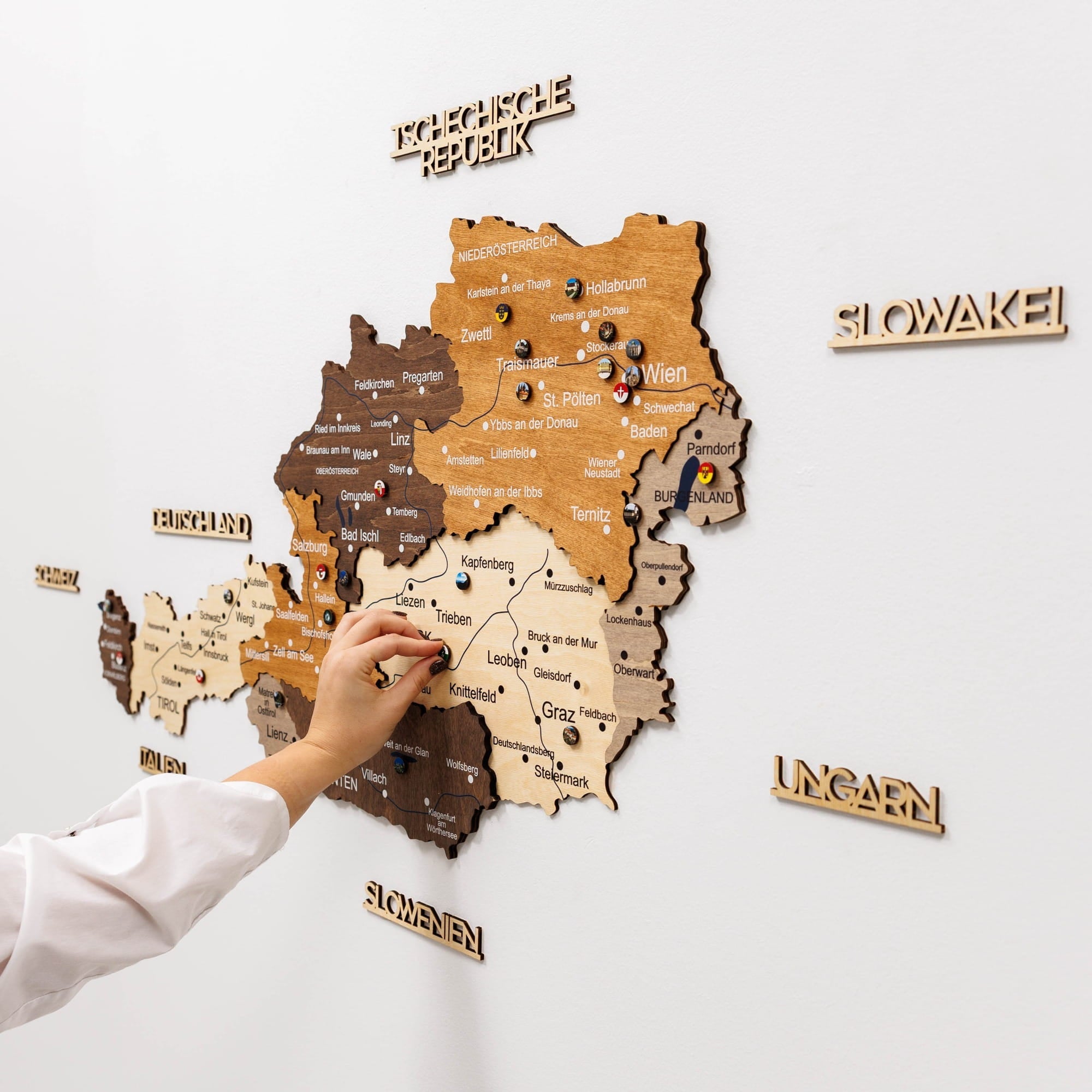 Wooden map of Austria with a hand pointing to a location on a white wall.