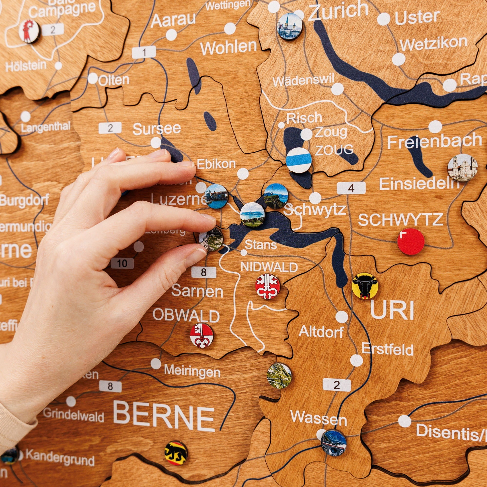 Wooden map of Switzerland with pins and a hand interacting with it