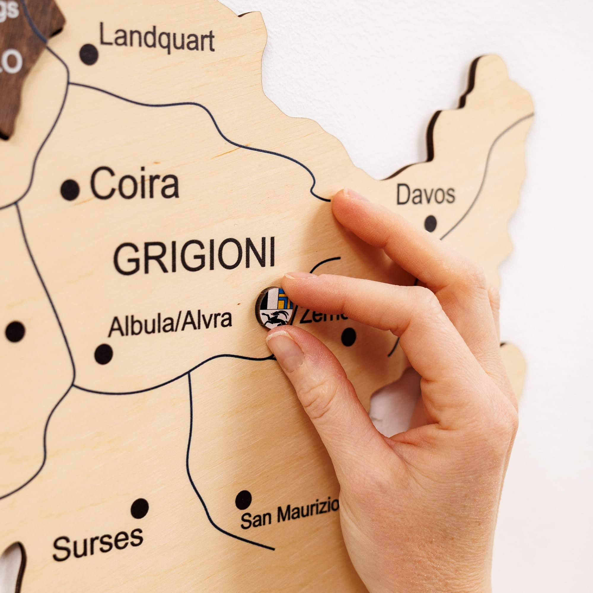 Hand placing a sticker on a wooden map of Grigioni, Switzerland.